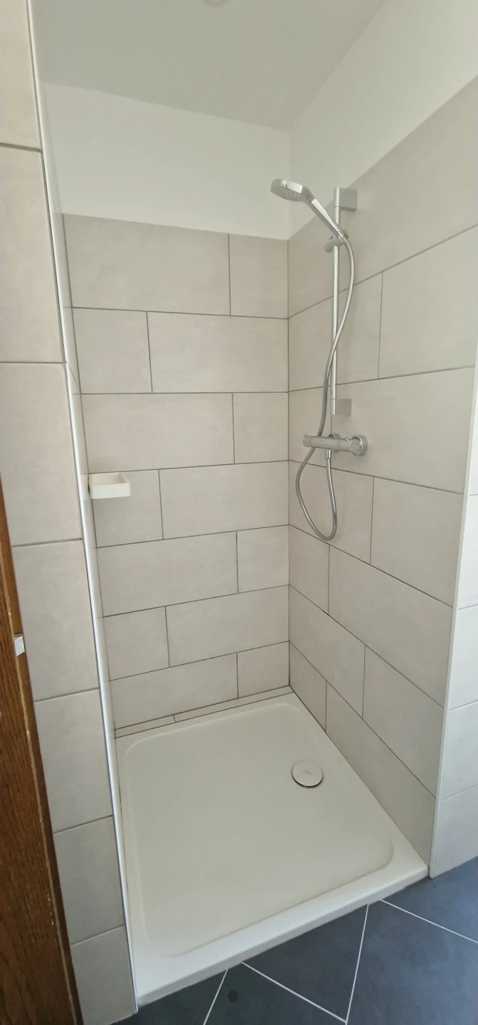 Fertig geflieste helle Dusche mit Duschwanne und Glasabtrennung