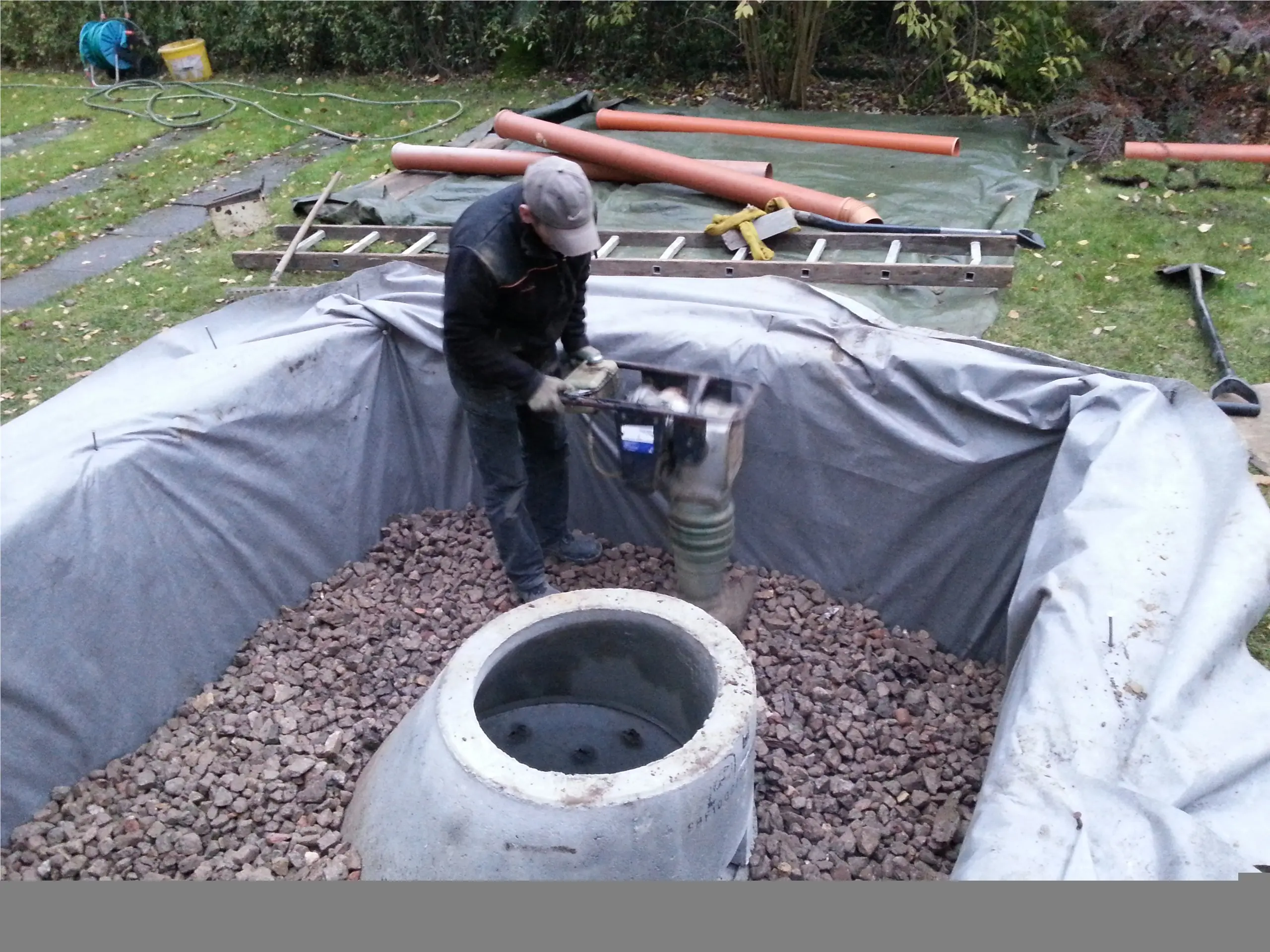 Mitarbeiter verdichtet Drainagematerial rund um mehrere Schachtteile